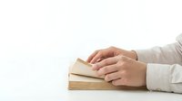 Hands resting on stack of books against white background, studying and education concept for academic learning and knowledge acquisition.