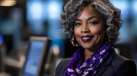 Confident mature African American businesswoman wearing purple floral scarf and black blazer smiling at camera in modern corporate office setting.