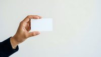 Hand holding blank white business card against neutral background, suitable for branding, corporate identity, and marketing mockup presentations.
