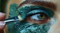 Close-up of eye with metallic emerald green eyeshadow being applied with makeup brush. Artistic beauty cosmetics showing professional application technique.