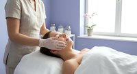 Professional spa therapist performing relaxing facial massage treatment on young woman client in modern wellness center with natural lighting and serene atmosphere.