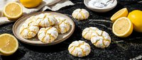 Homemade lemon crinkle cookies with powdered sugar on rustic wooden table. Fresh citrus baking ingredients and traditional dessert for tea time.
