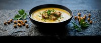 Creamy chickpea soup with herbs and spices served in black bowl on dark slate surface, garnished with fresh parsley and roasted chickpeas for healthy dining.