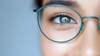Close up view of green eyeglasses frame and bright eye with long eyelashes against soft blue background, demonstrating optical care and vision correction.