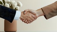 Professional business handshake between man and woman against neutral background with decorative white flowers in terracotta vase, symbolizing partnership and agreement.
