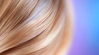 Smooth flowing blonde hair strands on blurred purple and blue gradient background, close-up view showing silky texture and natural highlights for beauty and haircare concepts.