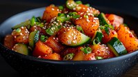 Fresh spicy Asian style salad with sweet watermelon cubes, cucumber, sesame seeds and green onions in dark bowl, close up view on black background.
