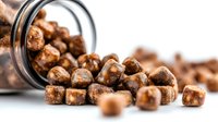 Chocolate coated cereal pieces spilling from glass jar on white background, perfect for breakfast food advertising and packaging design.
