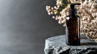 Dark amber glass bottle with pump dispenser on stone surface against blurred background with delicate white flowers, creating luxurious spa or cosmetic product scene.