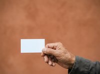 Senior male hand holding blank white business card against warm terracotta background. Suitable for corporate identity, networking, professional services, and business presentation designs.