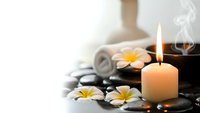 Spa wellness scene with burning candle, plumeria flowers and hot stones for relaxation massage therapy and aromatherapy treatment sessions.