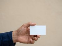 Male hand holding blank white business card against neutral beige background, suitable for branding, corporate identity, and marketing mockup designs.