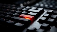 Close-up of computer keyboard with glowing red key illuminated in dark environment for technology and cybersecurity concepts.