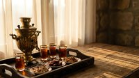 Traditional Russian samovar with tea glasses and sweets on wooden tray, cozy interior setting with warm sunlight streaming through curtains.