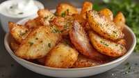 Crispy roasted potato wedges seasoned with herbs and spices served on ceramic plate with sour cream dip and fresh parsley garnish, close up view of appetizing side dish.