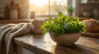 Fresh mint leaves in rustic wooden bowl on kitchen table with warm sunlight streaming through window creating cozy cooking atmosphere for culinary herbs.
