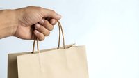 Hand holding eco-friendly brown paper shopping bag with handles against white background for retail and sustainable shopping concepts.