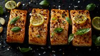 Grilled salmon fillets garnished with fresh basil leaves, lemon slices, and peppercorns on dark background, culinary presentation of seafood main course.
