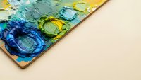 Artist palette with thick oil paint blobs in vibrant blue, green and yellow colors on wooden surface for creative painting and art projects.