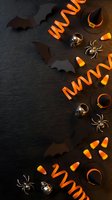 Halloween decorations with orange ribbons, black paper bats, candy corn, witch hats and spiders on dark slate background for seasonal party planning.