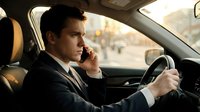 Professional businessman talking on phone while driving car in urban setting during daytime commute for business communication concepts.