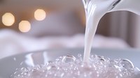 Pouring white liquid onto ice cubes creates dynamic splash effect with soft bokeh lights in background, capturing refreshing beverage moment in macro photography.