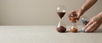 Hands arranging colorful hourglasses on neutral surface showing time management and productivity concepts for business planning.
