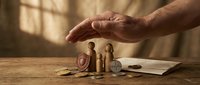 Protective hand covering wooden family figures with coins and documents on table, symbolizing financial security and insurance planning for loved ones.