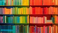 Colorful bookshelf arranged in rainbow spectrum order from blue and green to orange and red books, creating vibrant gradient pattern in library or bookstore.