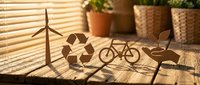 Eco-friendly wooden cutouts featuring wind turbine, recycling symbol, bicycle and leaves on sunny windowsill with plants, promoting sustainable living concepts.