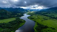 Aerial view of winding river through green valley with dramatic cloudy sky and mountains. Scenic landscape perfect for nature and travel projects.