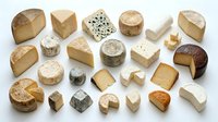 Assorted gourmet cheese collection featuring various artisanal varieties including soft brie, aged cheddar, blue cheese and goat cheese on white background.