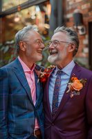 Senior male couple in stylish suits sharing joyful moment at their wedding celebration, wearing boutonnieres and colorful attire against urban backdrop.