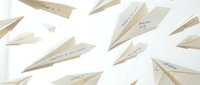 Paper airplanes with handwritten motivational messages scattered on white background for business inspiration and goal achievement concepts.