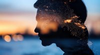 Male silhouette profile with double exposure effect showing starry night sky and city lights at sunset, creative portrait against blurred urban background.