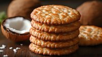 Stack of golden brown coconut cookies with fresh coconut and flakes on rustic wooden background, macro food photography showing crispy texture and details.