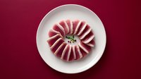 Fresh tuna sashimi slices arranged in circular pattern on white plate against burgundy background for culinary presentation and restaurant menu design.