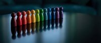 Colorful wooden peg people figures arranged in rainbow spectrum on reflective surface representing diversity, inclusion, teamwork and unity concepts.