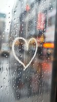Heart drawn on rainy window with blurred city lights in background, water drops streaming down glass creating romantic atmospheric mood on gloomy day.