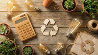 Wooden calculator, recycling symbols, glass bottles, and potted plants arranged on rustic wood surface for sustainability and eco-friendly business concepts.