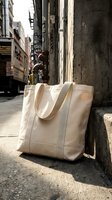 Beige canvas tote bag on urban street sidewalk against concrete wall with natural sunlight shadows for eco-friendly shopping and sustainable lifestyle.
