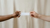 Two people of different ethnicities exchanging a blank white card or envelope against a neutral beige fabric background, symbolizing communication, agreement, or transaction.