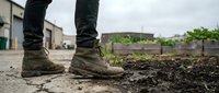 Unrecognizable person wearing muddy boots standing on dirt ground in rural outdoor setting, agricultural work environment.