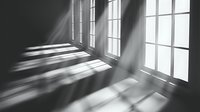 Dramatic sunlight streaming through large windows casting geometric shadows on empty room floor and walls, creating atmospheric light and shadow patterns in monochrome.