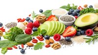 Fresh organic superfoods collection with avocado, berries, nuts, seeds and leafy greens arranged on white background for healthy nutrition concepts.