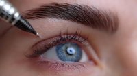 Permanent makeup procedure on eyebrow with cosmetic tattoo pen. Close-up of blue eye and perfectly shaped brow during microblading treatment.