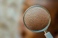 Magnified view of textured brown surface through circular magnifying glass showing detailed pattern of cracks and ridges against blurred background.