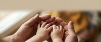 Adult and child hands forming protective circle together showing family care, support and unity in warm indoor setting.