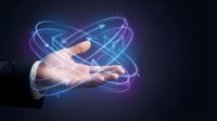 Hand holding glowing digital atom symbol with blue and purple neon light trails on dark background, representing science, technology, innovation, and atomic energy research.