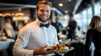 Smiling Caucasian male waiter in formal attire holding plate with gourmet meal in upscale restaurant setting with blurred dining room background and ambient lighting.